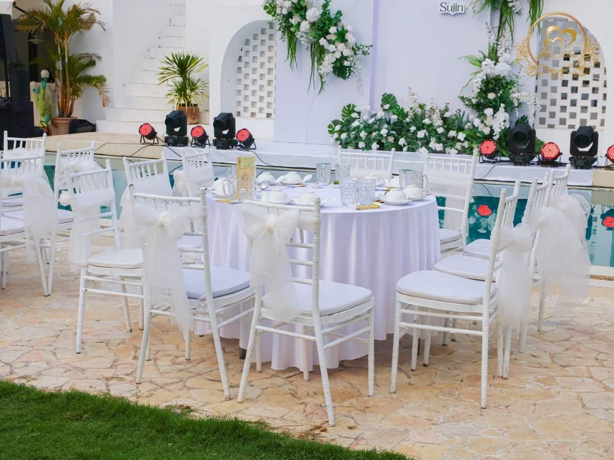 Setup bàn tiệc tròn ghế tiffany thắt nơ voan trắng bên hồ bơi.