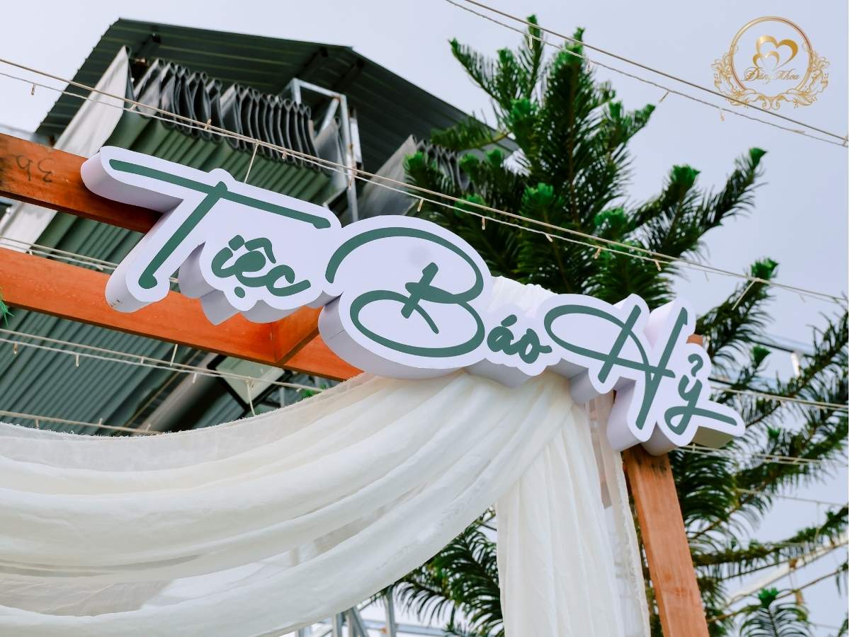 Cổng chào Tiệc Báo Hỷ thiết kế khung gỗ Rustic kết hợp hoa lụa trắng và lá xanh.