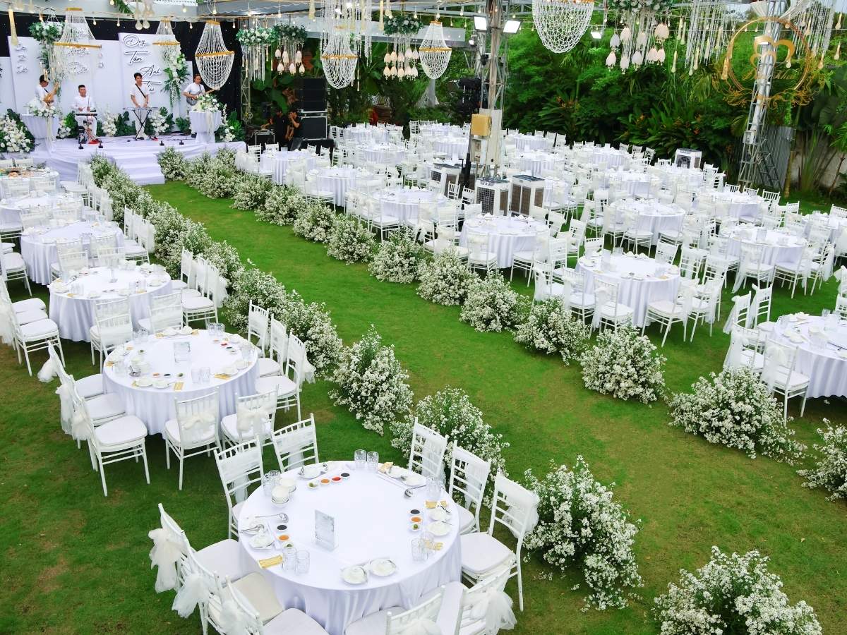 Toàn cảnh không gian Tiệc Báo Hỷ với lối đi viền hoa baby trắng lộng lẫy và bộ bàn ghế Tiffany tone trắng đồng bộ.