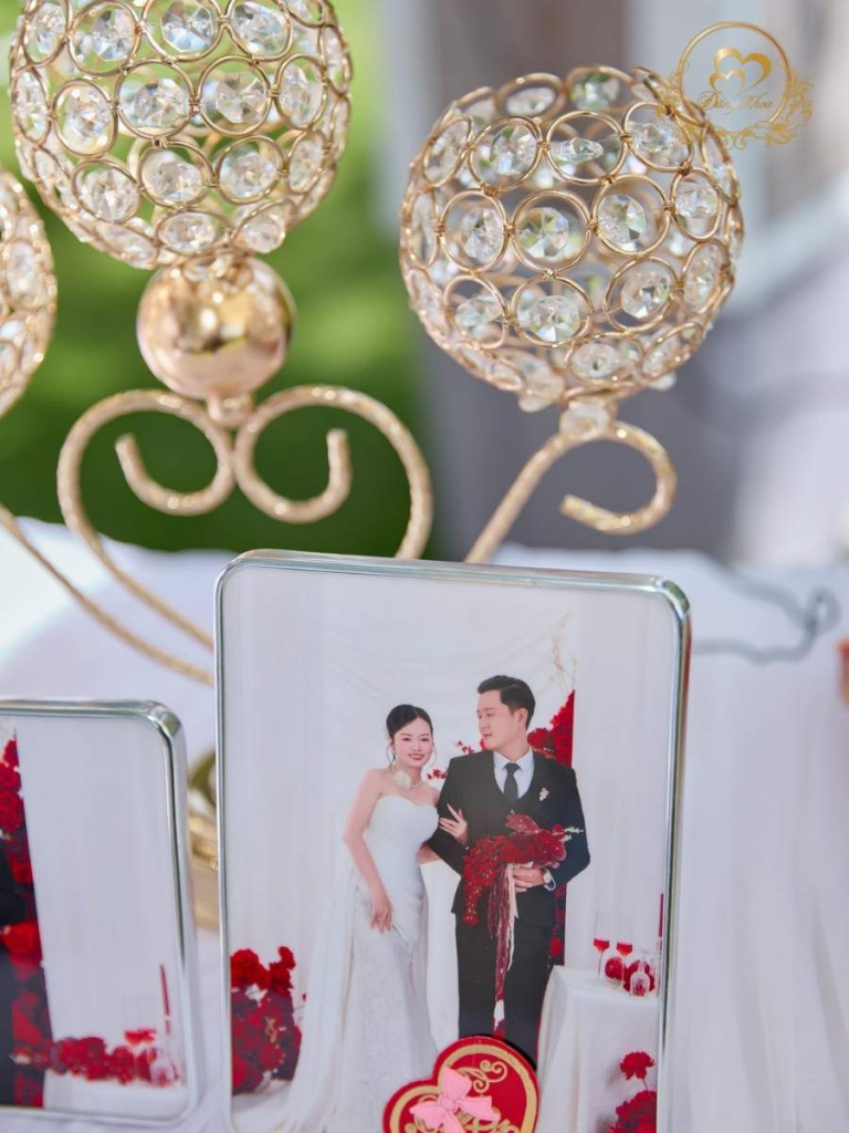 Chi tiết phụ kiện bàn đón khách: trụ nến gold và ảnh cưới chú rể cầm hoa đỏ