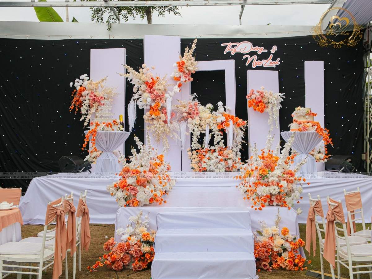 Sân khấu chính tiệc cưới tone cam với phông nền màn sao đen huyền ảo.