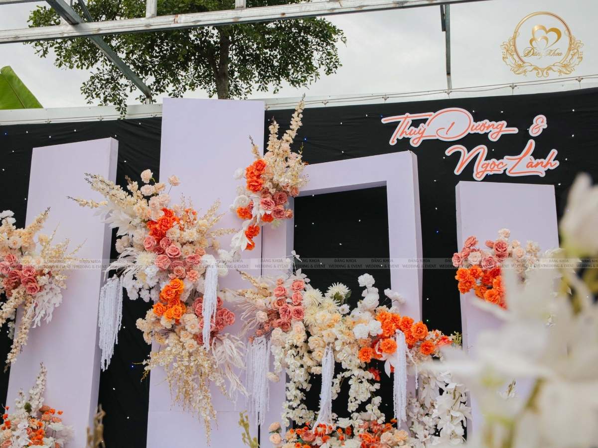 Cận cảnh backdrop sân khấu đám cưới tone cam với tên cô dâu chú rể nổi bật.