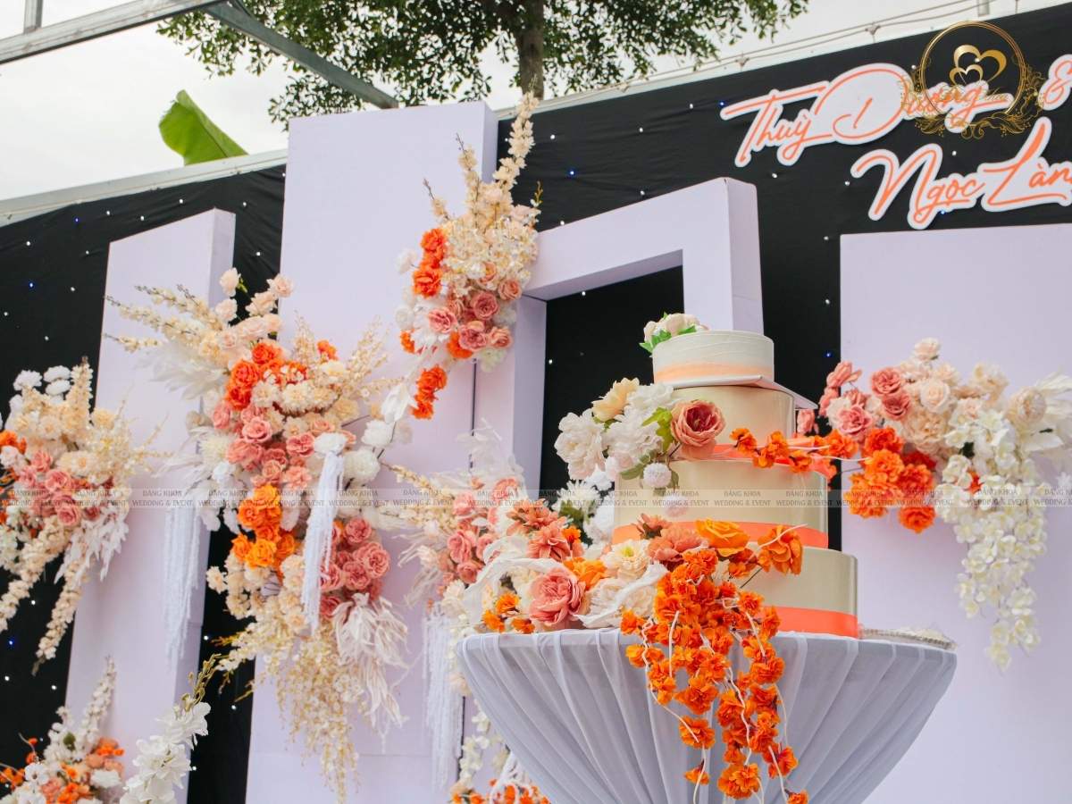 Bánh kem cưới nhiều tầng trang trí hoa tươi tone cam đồng bộ với concpet.