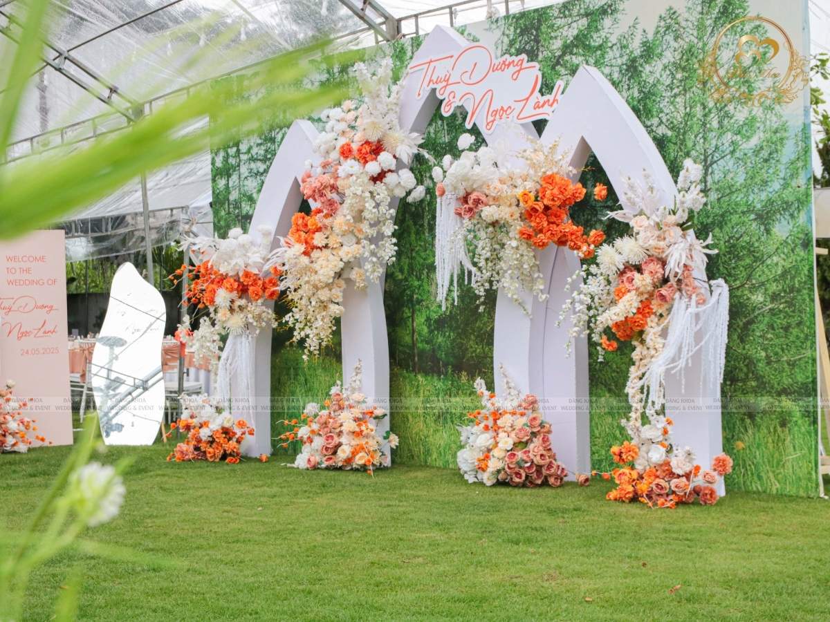 Backdrop chụp hình cưới đón khách thiết kế vòm nhọn kết hoa cam rực rỡ.