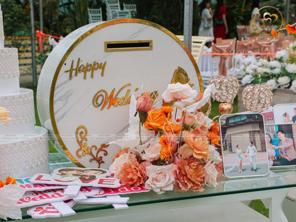 Chi tiết trang trí bàn Gallery thùng tiền lục giác, khung ảnh và hoa hồng cam.