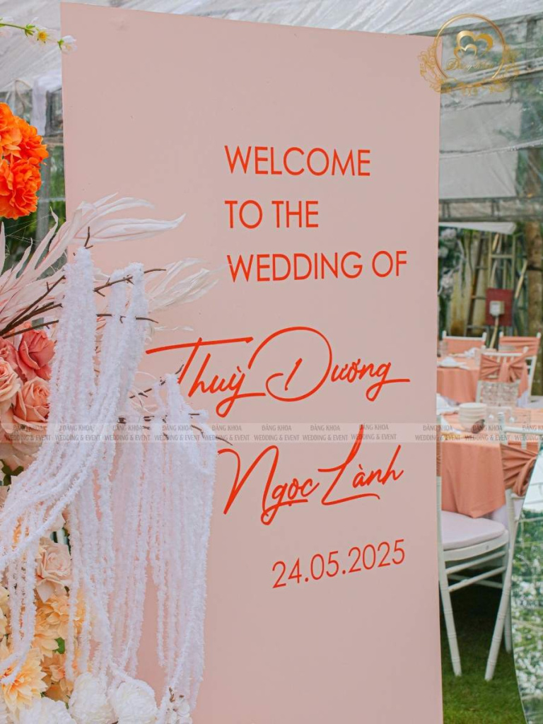 Khu vực bảng Welcome đón khách trang trí hoa tươi tone cam rực rỡ.