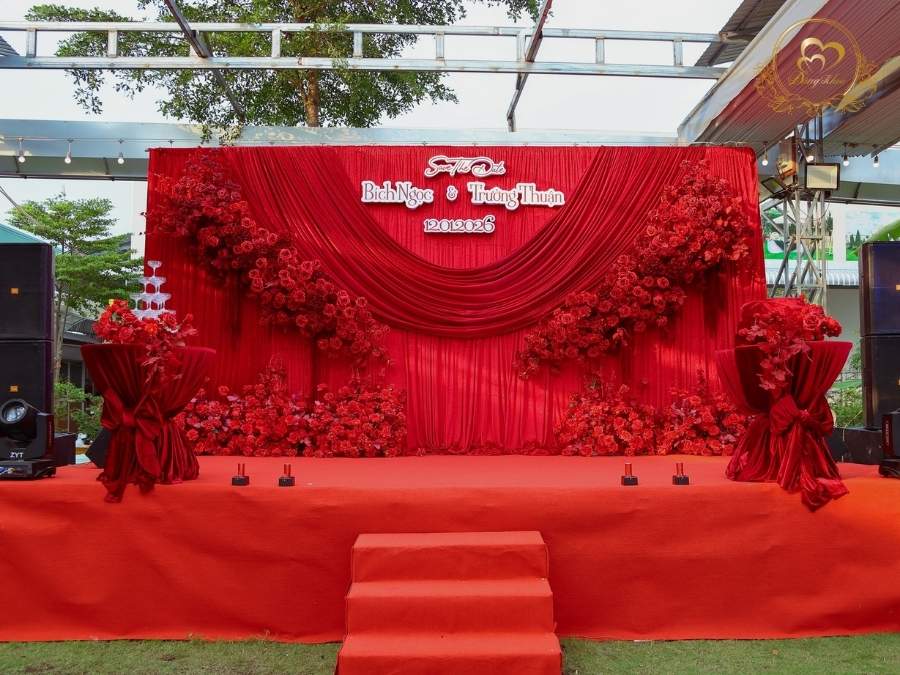 Sân khấu Save The Date tone đỏ nhung & tháp ly champagne sang trọng.