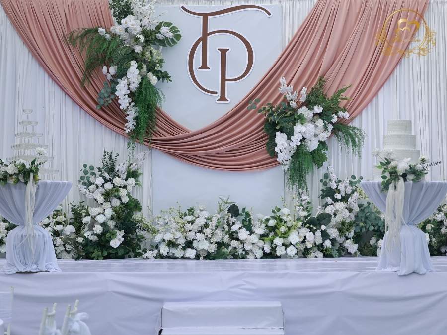 Toàn cảnh sân khấu Happy Wedding T&P logo chữ cái lồng và tháp ly và bánh kem sang trọng.